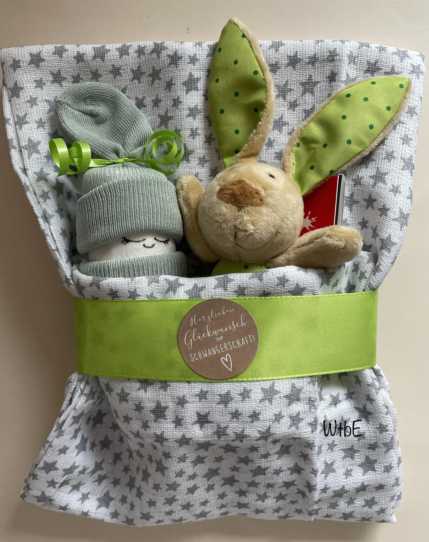a baby diaper and a rattling rabbit toy placed on a cloth, unisex color, green and gray