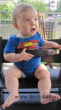 baby girl sitting in a highchair wearing a superman onesie